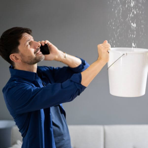Worried business owner catching water from a ceiling leak with a bucket while calling Roofing Guys Central Coast, experts in fast commercial roof leak detection and repairs. Worried business owner catching water from a ceiling leak with a bucket while calling Roofing Guys Central Coast, experts in fast commercial roof leak detection and repairs.